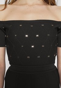 Haut noir à épaules dénudées avec un tricot texturé, un motif en diamants et des accents métalliques, doté de manches courtes et d'une taille cintrée.