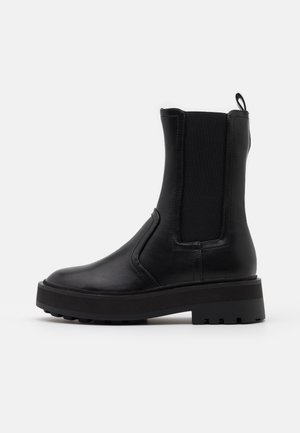 Schwarzer Leder-Stiefelette mit elastischen Seitenteilen, abgerundeter Spitze und klobiger Gummisohle. Verfügt über eine Schlaufe an der Rückseite für einfacheres An- und Ausziehen.