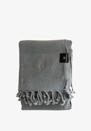 Sivý tkaný textil zložený s skrútenými strapcami na jednom okraji a čiernou nálepkou prišitou blízko okraja.