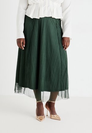 Mørkegrøn plisseret midi-nederdel båret med hvid bluse og beige højhælede sko med ankelstropper og dekorative spænder.