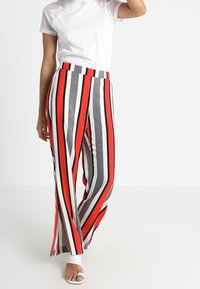 Pantalones de pierna ancha a rayas en tejido rojo, negro, gris y blanco; presentan una cintura alta y una silueta fluida. Combinados con una camiseta blanca.