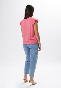Top rosa a maniche corte con spalle arricciate, tessuto strutturato, abbinato a jeans in denim azzurri a vita alta e sandali con tacco beige.