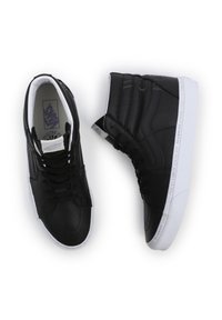 Mustat nilkkurit, jotka on valmistettu nahasta, jossa on sileä pinta, valkoinen kumipohja ja tunnuslogo kielellä ja pohjassa.