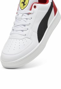 Vit lågtoppad sneaker med svart rand, röd häl, vita snören och en gul Ferrari-logotyp på tungan.