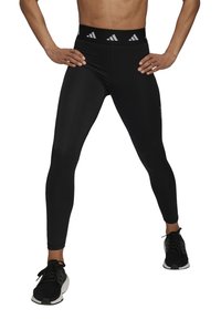 Svarta träningstights med hög midja och vita Adidas-logotypdetaljer. Tillverkade av elastiskt material, åtsittande design, ankellängd.