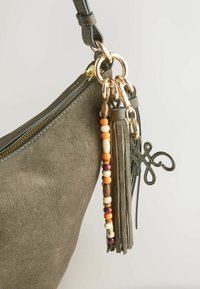 Sac à main en daim vert olive avec quincaillerie dorée, pompon perlé, franges en cuir cousues et breloque boucle en cuir décorative sur l'anneau de la sangle.