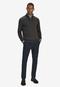 Miestenska tmavošedá zipovacia mikina, námornícke nohavice a hnedé topánky. Mikina má rebrovaný lem a manžety. Tričko pod ňou je svetlomodré.