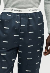 Σκούρα μπλε boxer Calvin Klein με επαναλαμβανόμενα λευκά λογότυπα και λευκή ελαστική ζώνη μέσης με την επωνυμία Calvin Klein.