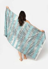Handdoek met een strand geïnspireerd ontwerp met afwisselende turquoise en grijze strepen, en zwarte palmen bladeren patronen, afgewerkt met franjes.