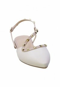 Scarpa piatta bianca a punta con una cinghia incrociata color nude, decorata con borchie dorate lungo la cinghia, caratterizzata da una superficie liscia.