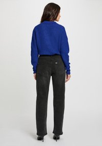 Suéter de punto azul con un corte relajado, tejido texturizado y mangas largas; combinado con jeans negros de talle alto y zapatos de tacón negros.