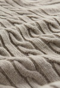 Bežna pletena tkanina s uzorcima uzdignutih valova, meke teksture i vidljivim vlaknima, koja stvara ugodan i taktilan izgled.