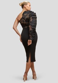 Sort midi-kjole med blonder overkrop med asymmetrisk design, et flæset ærme og en sidelomme. Glat, tætsiddende silhuet.