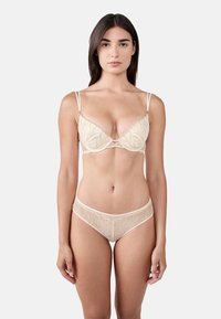 Beige lace bralette with delicate leaf patterns, adjustable straps, and matching sheer brief with similar embroidery details.