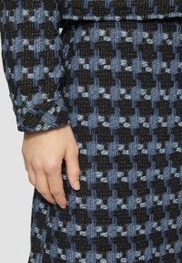 Zwart en blauw gestreepte stof met een gestructureerde weving, met een rasterachtig ontwerp. Een hand is op de stof geplaatst, om de details te tonen.