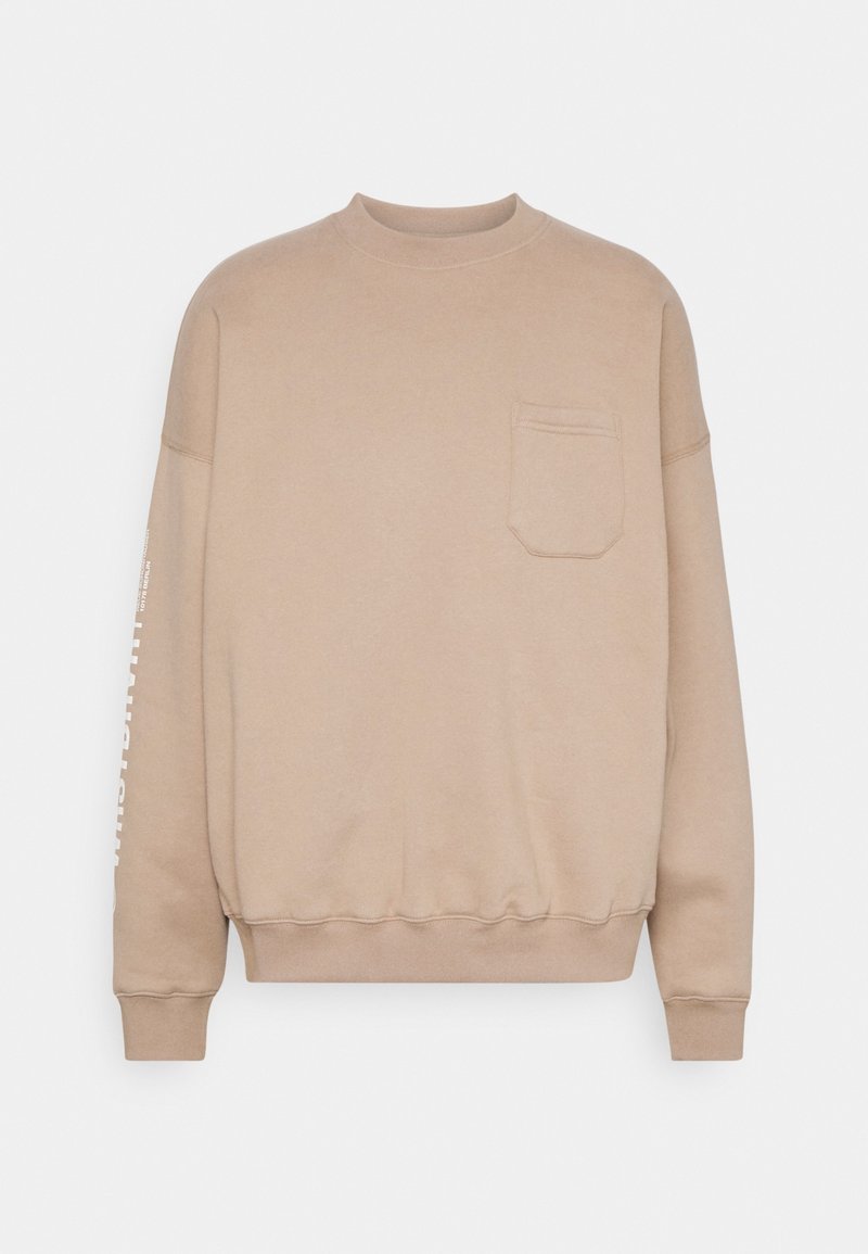 Sweat-shirt beige à col rond avec manches longues, une poche poitrine frontale, des poignets et un ourlet côtelés, et un texte blanc imprimé partiellement visible sur la manche gauche.