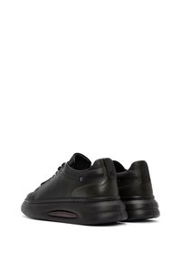 Sneaker in pelle nera con talloni arrotondati, suole curve e cucitura decorativa. Presenta una sezione in air cushioning trasparente.