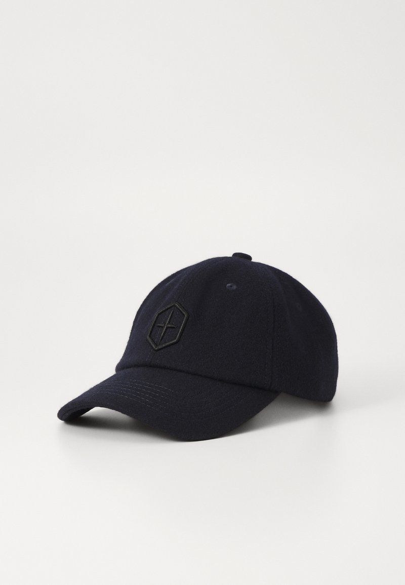 Gorra de lana en color marino con visera curva, que presenta un logotipo hexagonal negro en la parte frontal y una superficie de tela texturada.