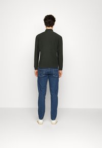 Polo de manga larga verde oscuro combinado con jeans de mezclilla azules, con costuras en los bolsillos traseros y zapatillas blancas.