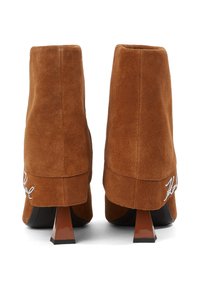 Stivaletti in suede marrone con tacco alto, caratterizzati da un design architettonico unico. Presentano una texture liscia e dettagli ricamati sulla parte posteriore.