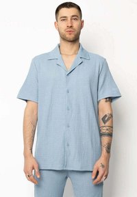 Chemise à boutons bleu clair à manches courtes en tissu texturé, avec un col pointu et des boutons bleu. Convient pour un style décontracté.