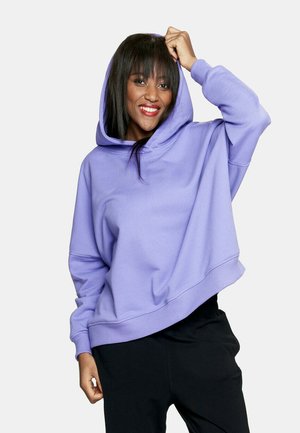 Jasnofioletowa, oversize'owa bluza z kapturem regulowanym sznurkiem, z prążkowanymi mankietami i dołem, w zestawie z czarnymi spodniami. Gładka faktura, swobodny design.
