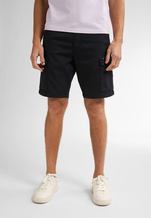 Sorte cargo shorts lavet af bomuldsblanding, med sidelommer, opsmøgede kanter og en afslappet pasform. Båret med hvide sneakers.