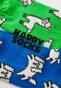 Chaussettes colorées avec un haut vert orné d'illustrations de chiens blancs et un bas bleu affichant le texte "HAPPY SOCKS", le tout avec des motifs ludiques.