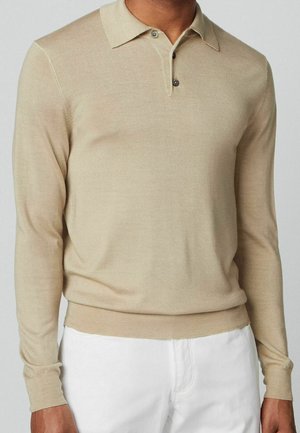 Pull polo beige à manches longues en maille lisse et légère ; doté d'un col classique et d'une patte à deux boutons avec des boutons foncés.