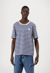 Camiseta de manga corta a rayas con rayas horizontales en azul y blanco, cuello redondo y un pequeño detalle de logo blanco en el pecho.