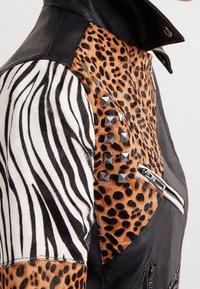 Giacca di pelle nera con pannelli a stampa zebra e leopardo, borchie argentate e tasche con zip. Texture distintiva e modelli audaci.