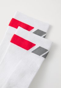 Calcetines blancos con acentos en rojo y gris, con un tejido texturizado y rayas audaces cerca de la parte superior y formas de diamante en el costado.