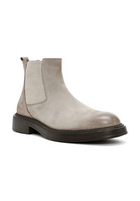 Bota Chelsea de ante topo con paneles laterales elásticos, punta redonda y una suela negra texturizada y baja. Cuenta con una lengüeta para facilitar su uso.