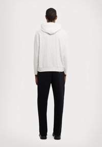 Hanorac alb cu modele geometrice, având glugă cu șnur și manșete ribbadate, combinat cu pantaloni negri și încălțăminte neagră.