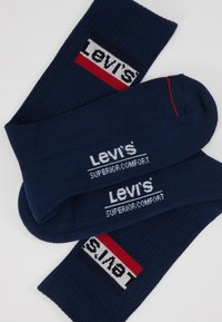 Sötétkék pamut zokni, kontrasztos fehér 'Levi's' logóval és piros részletekkel. Simaságával és bordázott szegélyeivel rendelkezik.