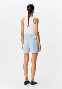Pantaloni corti azzurro chiaro con vita elastica e tasche posteriori, abbinati a una canotta bianca aderente. Tessuto morbido e liscio, design casual.
