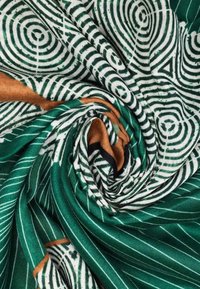 Tessuto verde e bianco con motivi a spirale, caratterizzato da disegni circolari e lineari con una lucentezza metallica e accenti marroni.