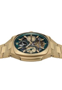 Gouden mechanische horloge met een groene wijzerplaat, ingewikkeld skeletontwerp, sub-wijzerplaat en een geborstelde gouden armband. Opvallende details zijn de blauwe accenten.
