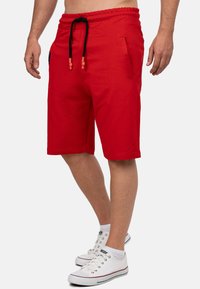 Rode katoenen shorts met een elastische tailleband en zwarte koordjes, met zijzakken en een rechte snit. Draagt een paar witte sneakers.
