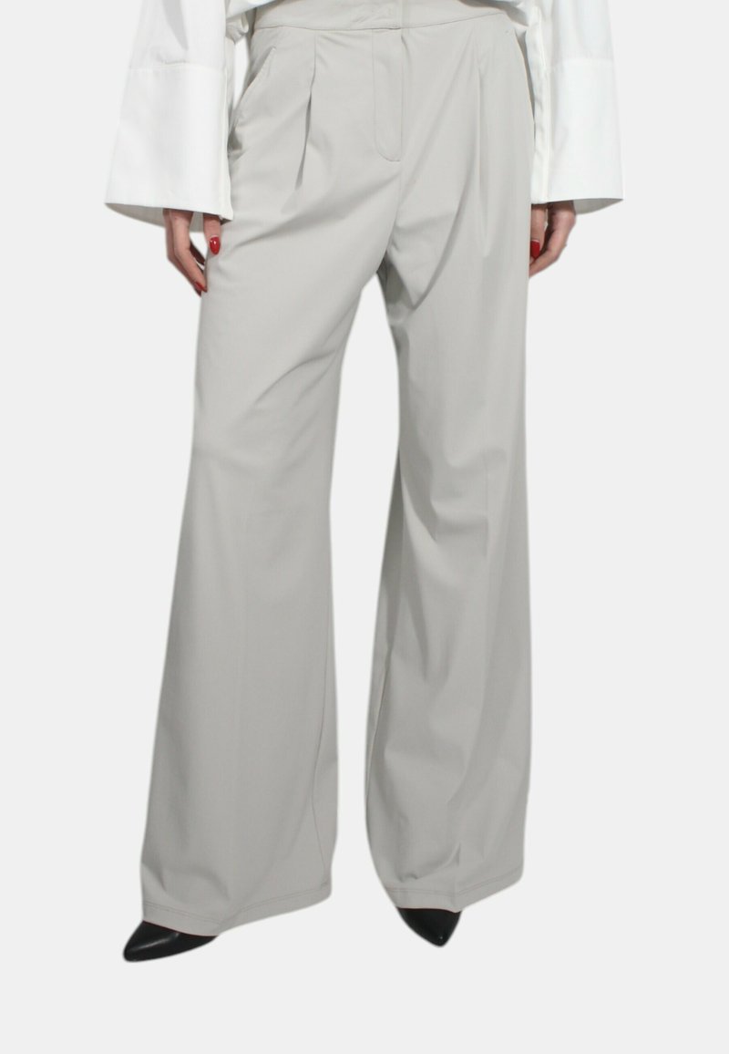 Pantaloni larghi grigi chiari con pieghe, realizzati in un tessuto morbido. Caratterizzati da una vita alta e un design sartoriale, abbinati a scarpe nere a punta.