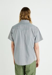 Camisa de manga corta en denim gris claro, con un collar estructurado y un dobladillo curvado. La parte trasera tiene detalles en el yugo y un corte relajado.