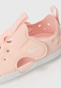 Nike papucs, puha rózsaszín gumiból, fehér logóval, kivágott dizájnnal, texturált talppal és állítható pánttal a biztonságos illeszkedésért.