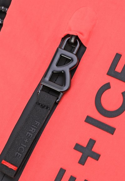 Rode stoffen tas met een opvallende zwarte rits en gesp met de letter "B." Inclusief textuuraccenten en merkdetails.