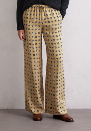 Weite Hosen aus gelbem Stoff mit schwarzen geometrischen Mustern, ausgestattet mit einem elastischen Bund und einer glatten Textur.