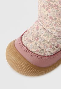 Nærbilde av en vinterstøvel med gummisåle, rosa skinn tåhette og stoffoverdel med et pastellblomstermønster.