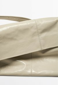 Beige leather bag with a glossy finish, featuring a large fold, visible stitching, and a simple design. Functional and flat shape.