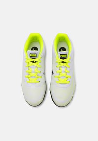 Zapatillas deportivas blancas con un upper texturizado, que presentan el logo negro de Puma, cordones y interior de color amarillo neón, y una suela de goma negra.