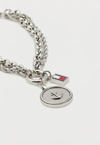 Ασημένιο βραχιόλι αλυσίδας με δύο γούρια: ένα στρογγυλό μετάλλιο με χαραγμένη άγκυρα και την επιγραφή «Tommy Hilfiger» και μια μικρή ορθογώνια σημαία.