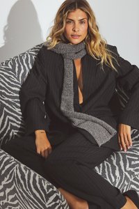 Black pinstripe suit with a gray scarf draped around the neck. The background features a zebra print sofa.