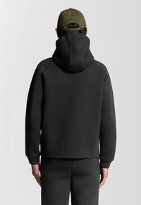 Svart huvtröja med slät textur och känguruficka. Har raglanärmar och en något kortad nederkant. Matchas med byxor i samma stil.